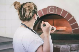 woman putting a pizza into a woodfire oven