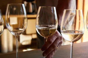 three glasses of white wine, one glass being held by a man's hand.