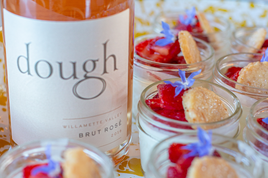 Bottle of Dough Brut Rose nestled next to strawberry shortcake dessert in mason jars